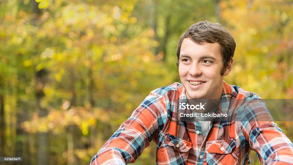 Lächelnde junge sitzt auf der Vorderseite von Bäumen mit Herbst Blätter - Lizenzfrei Zahnspange Stock-Foto