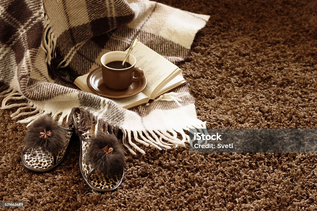 Comfortable still life Woolen plaid, coffee cup, book and slippers on shaggy carpet. Focus on slippers. Cozy Stock Photo