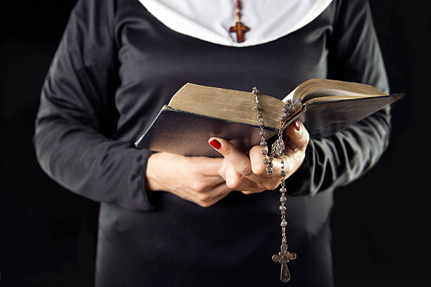 istock nun hands holding bible book over grey background 521684566