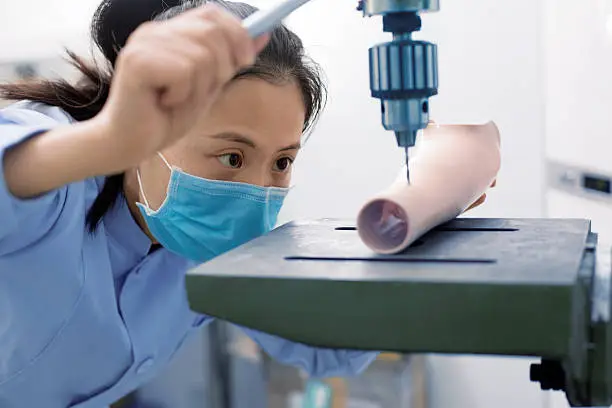 Photo of worker is using a drilling machine to process a prosthetic