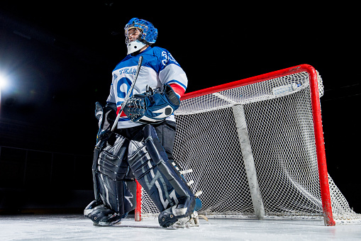 Ice hockey goalkeeper standing in front of ice hockey goal in ice hockey stadium, low angle view.