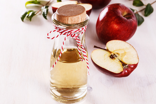 Apple cider vinegar and red apples over white wooden background. Selective focus