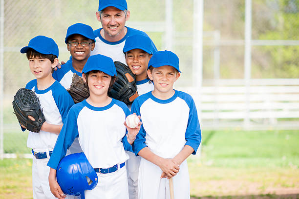 Holding the Home Run Ball A multi-ethnic group of elementary age boys are wearing their baseball uniforms and are together in a team huddle and are smiling and looking at the camera. men baseball baseball cap baseball bat stock pictures, royalty-free photos & images
