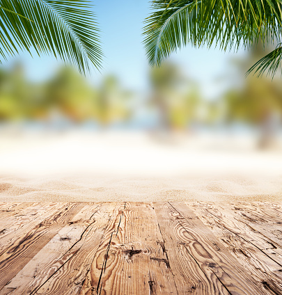 Empty wooden planks with blur beach on background, can be used for product placement, Palm leaves on foreground