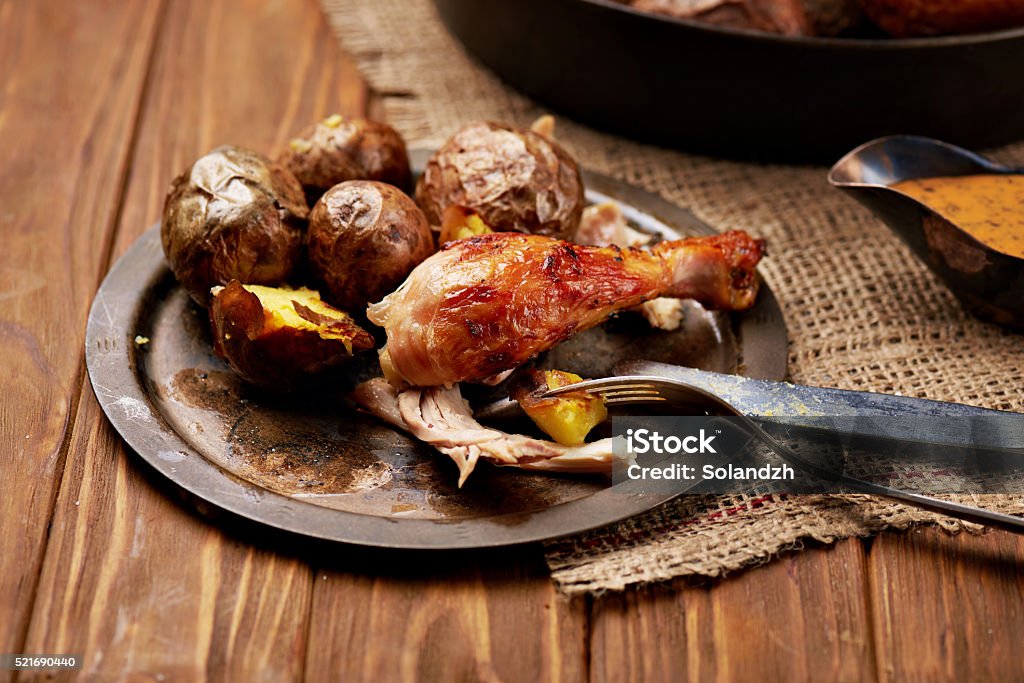 Barbecued chicken leg with baked potatoes Close view at barbecued chicken leg with baked potatoes on a rustic metal plate with whole chicken and sauce on a background. Sackcloth and wooden background. Warm colors Animal Body Part Stock Photo