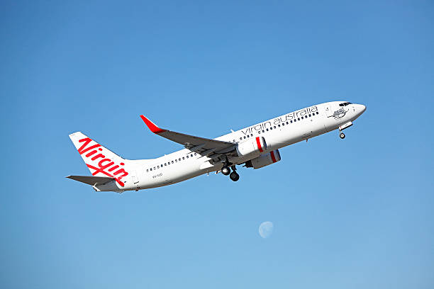 Virgin Over The Moon: plane taking-off with moonrise. Melbourne, Australia - April 17, 2016: Virgin Over The Moon: On a sunny autumn day, Virgin Boeing 737 VH-VUD “Tallow Beach” takes off from Melbourne’s Tullamarine Airport into clear blue skies as it heads to Sydney with a domestic service (VA895) on one of the world’s busiest air corridors.  It is seen passing over the rising moon.   aerodynamic photos stock pictures, royalty-free photos & images