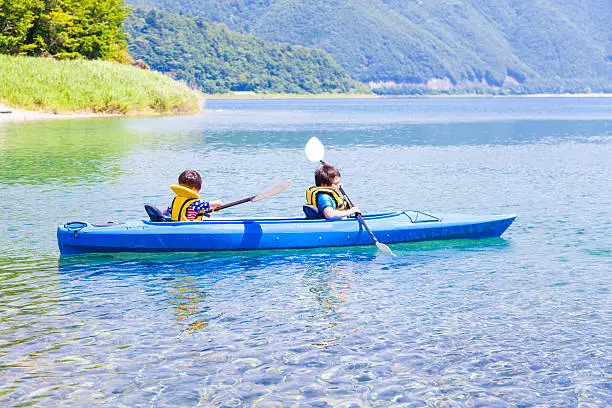 Boys paddling on the tandem kayak in the lake.