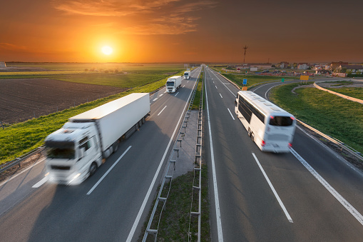 Many white trucks in line and fast travel bus driving towards the sun. Speed blurred motion drive on the freeway at beautiful sunset. Transport travel scene on the motorway near Belgrade, Serbia.