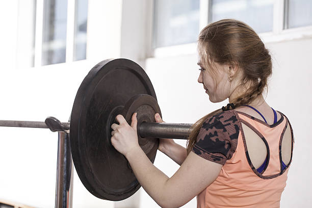 girl is engaged in sports exercises with a barbell. girl is engaged in sports exercises with barbell girl changes the weight on the barbell crossfit girl stock pictures, royalty-free photos & images