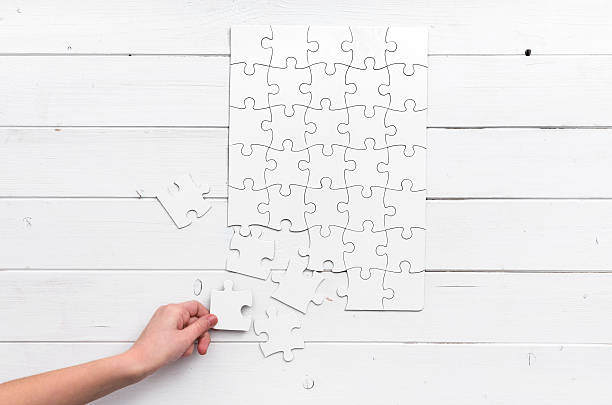 hand holding a piece of white uncompleted puzzle hand holding a piece of white uncompleted puzzle on white wooden background uncompleted stock pictures, royalty-free photos & images