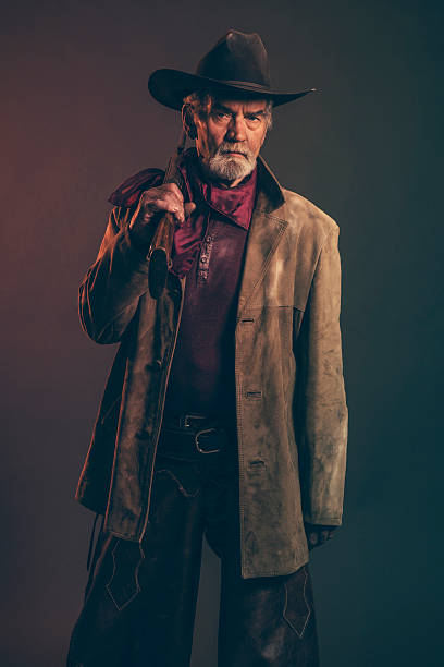 istock Senior cowboy with gray beard and brown hat holding rifle. 521708729