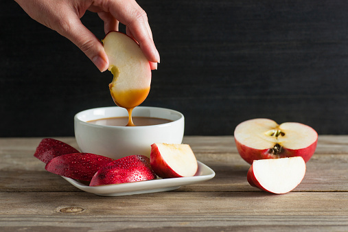 Woman's hand dipping a fresh apple slice into homemade salted caramel sauce.