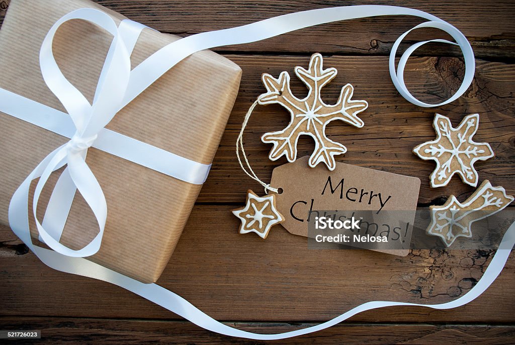 Merry Christmas Greetings with Gift and Cookies Merry Christmas Greetings on Natural Tag on Wooden Background Decorated with a Gift Box and Ginger Bread Cookies, Christmas Background Backgrounds Stock Photo