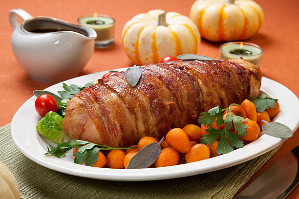 Bacon-wrapped Turkey Breast Roulade Delicious bacon-wrapped turkey breast roulade garnished with Brussels sprouts, tomatoes, and Parisian carrots. turkey breast stock pictures, royalty-free photos & images