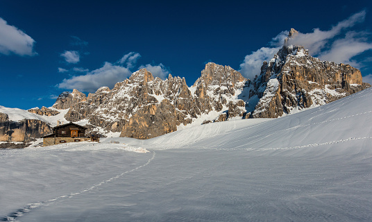 Baita Segantini mountain hut and the Pale of San Martino mountains in the snow in a winter day with blue sky with clouds, Dolomites, Italy