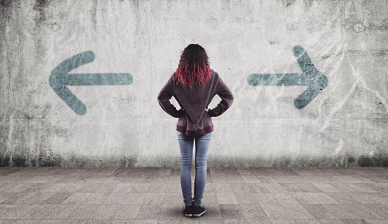Young girl in front of a wall painted with arrows towards opposite directions.  'left or right'