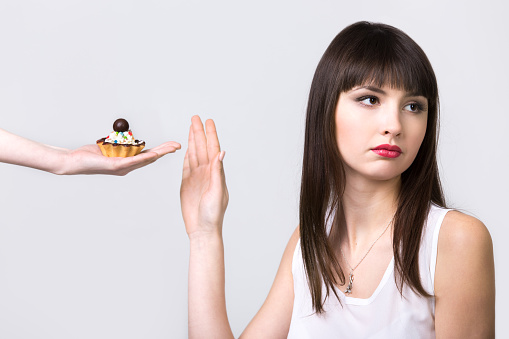 Young resolute dieting beautiful woman refusing tart cake with cream and chocolate, studio, healthy lifestyle concept, gray background, isolated