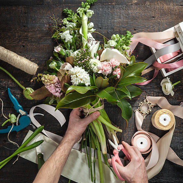 The hands of florist against desktop with working tools and ribbons on wooden background