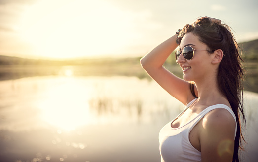 Portrait of smiley attractive woman by the lake at great sunset.She enjoys in nature on great sunny day.