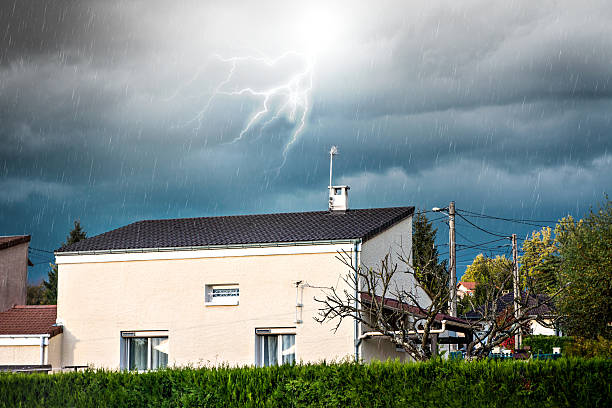 Outdoors of stormy weather, with rain trails in blurred motion and lightning from violent storm in autumn season, residential district with common white small house.