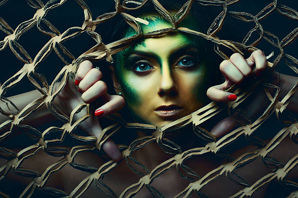 Woman behind net surreal woman with green face paint looking at camera behind net prison escape stock pictures, royalty-free photos & images