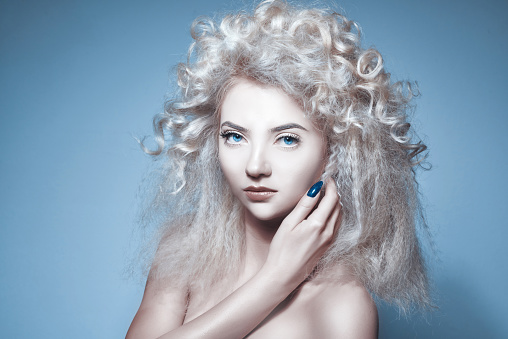 attractive blond hair woman touching her face, looking at camera and feeling seductive, posing in studio shot on blue background.