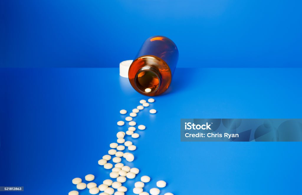 Prescription pills spilling out of bottle onto blue counter  Abundance Stock Photo