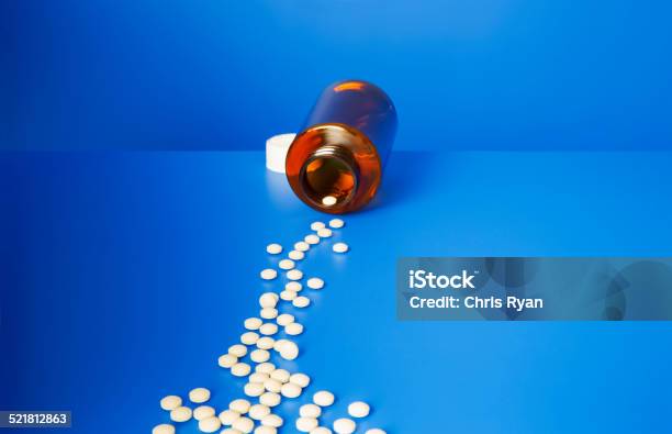 Prescription Pills Spilling Out Of Bottle Onto Blue Counter Stock Photo - Download Image Now