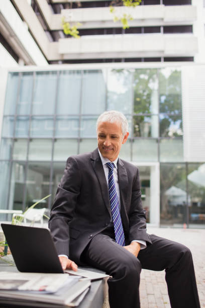 istock Businessman using laptop on bench outside of office building 521812913