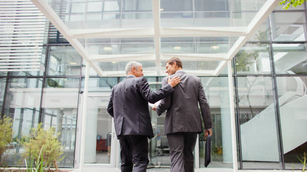 hombres de negocios que entran juntos al edificio de oficinas - business two people talking building exterior fotografías e imágenes de stock