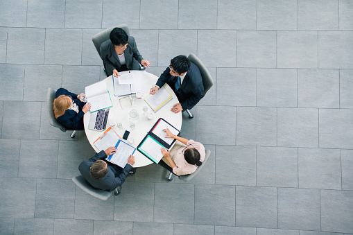 From above photo of unrecognizable team of six multi-ethnic employee reading and typing business report on laptop computers and digital tablet while sitting together at office desk.