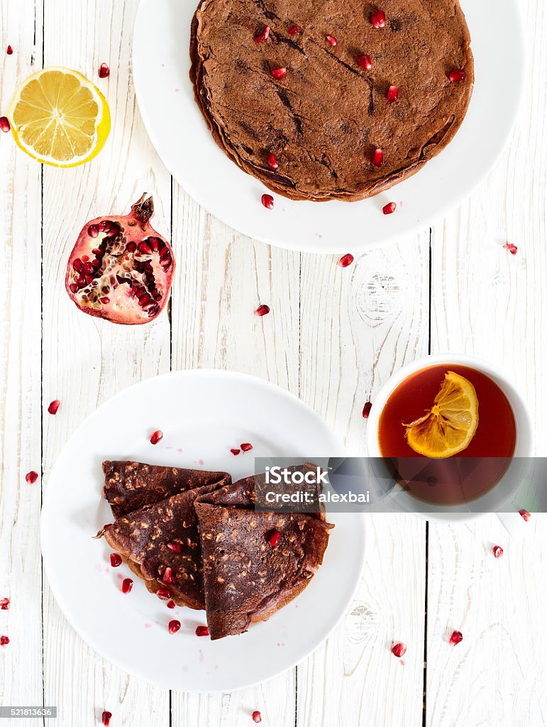 Chocolate crepes with oatmeal Chocolate crepes or pancakes with oatmeal and pomergranate. White wood table with healthy homemade sugar and eegs free breakfest dish on white plate, with a cup of tea with lemon and pomegranate near Crêpe - Pancake Stock Photo