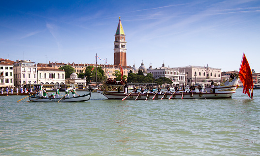 Venice, Italy - May 17, 2015:  Gondoliers participate in the Festa della Sensa, an annual spring festival celebrating the symbolic marriage of Venice to the Sea. Boats and gondolas parade and race from St. Mark's Basin (pictured here) to the Lido. The Venetian flag is visible on the antique boat on the right. 