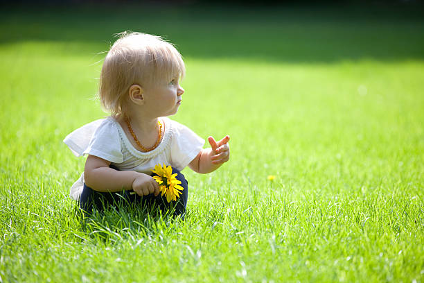 istock Baby Girl Playing with Flower Outdoors on Grass Pointing 521817373