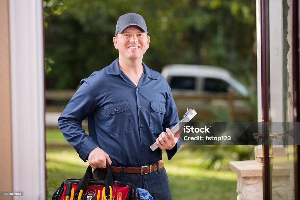 Service Industry: Repairman at customer's front door. Caucasian repairman or blue collar/service industry worker makes service/house call at customer's front door. He holds his clipboard and tool box filled with work tools. Inspector, exterminator, electrician. He wears a navy blue uniform. Service truck seen in background parked on road.  Electrician Stock Photo