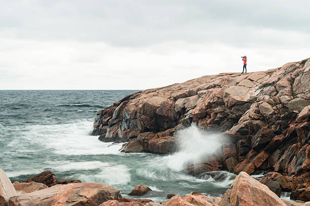 Nature photographer on coastline, woman photographing Nature photographer on coastline. Woman photographing in a wild area on top of rocks near ocean. cabot trail stock pictures, royalty-free photos & images