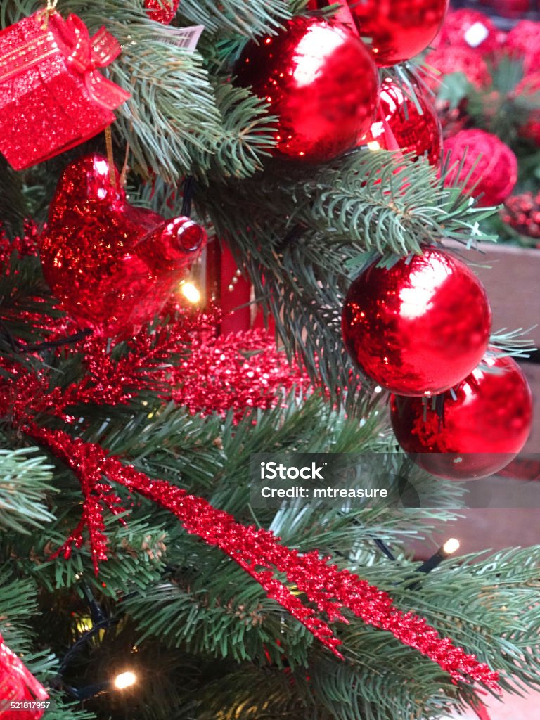 Artificial Christmas tree, red decorations, garlands, baubles, tinsel, parcels, fairy-lights Photo showing an artificial Christmas tree with green plastic spruce needles, and themed red decorations.  These xmas decorations include garlands of red tinsel, glittering foliage and chains, as well as white fairy lights, small wrapped parcels and shiny, sparkling baubles. Artificial Stock Photo