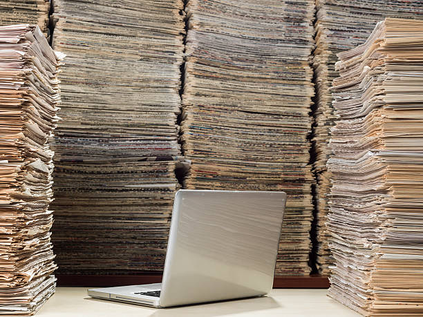 istock Laptop among huge stack of documents and books in library 521818053