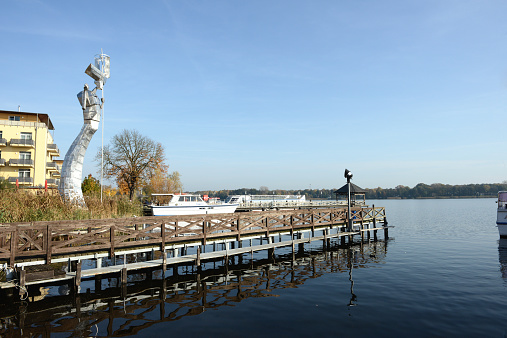 Neuruppin, Germany - November 1, 2014: Ruppiner Lake with pier and art figure at town Neuruppin (Ostprignitz-Ruppin, Germany) during autumn time. The figure made of metal was created by Matthias Zágon Hohl-Stein and one of the sightseeing item of the town.
