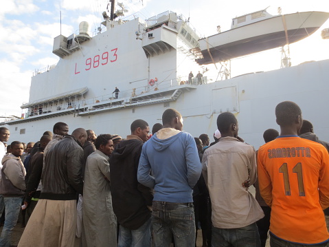 Augusta, Sicily, Italy - December 11, 2013: Migrants stand in line at the Sicilian harbour of Augusta, near the Amphibious warfare ship San Marco.