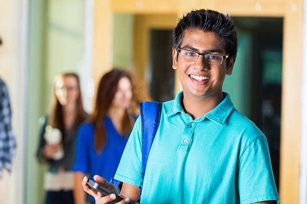 istock Happy Indian high school student using phone outside classroom 521849589