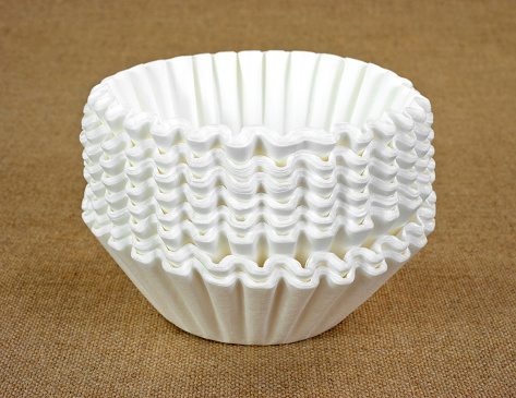 A stack of new white coffee filters on a tan cloth background.
