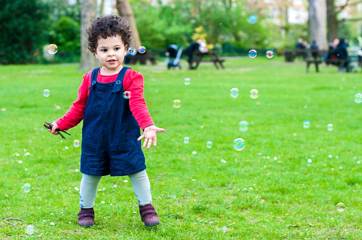Stock Photo of child aged 2 years old who is enjoying catching bubbles flying around her in the local park. Shot in Raw and post processed in ProPhoto RGB. No sharpening applied. This file has a 