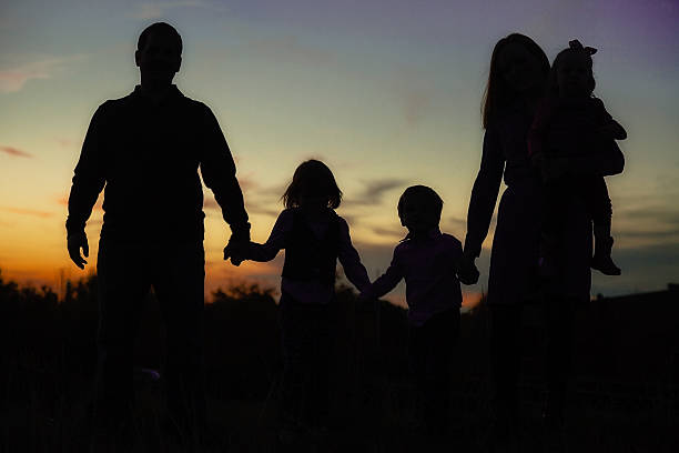 Young Family Hand-in-Hand Silhouette with Vibrant Sunset in Background stock photo