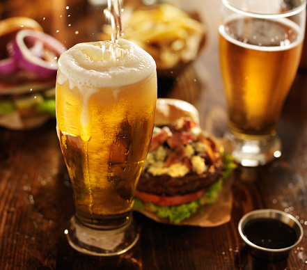 beer being poured into glass with gourmet hamburgers on pub table.