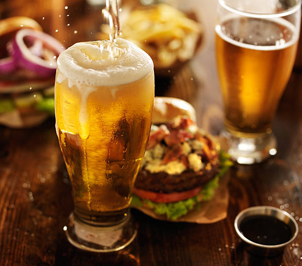 beer being poured into glass with gourmet hamburgers stock photo