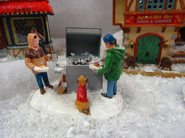 Image of model Christmas village , miniature houses, people, winter-bbq Frome, Somerset, England, UK - November, 1 2014: Seasonal concept photo showing a magical model Christmas village scene in winter set up in the conservatory of my house, using a large table, wooden staging and white polyester fleece to create a blanket of snow.  The model village recreates a detailed winter's scene in miniature and comes complete with miniature ceramic buildings and houses, realistic plastic, hand-painted people and scale figurines - such as a family using a winter barbecue / bbq surrounded by snow (all made by Lemax) and lots of fake snow powder. charles dickens stock pictures, royalty-free photos & images