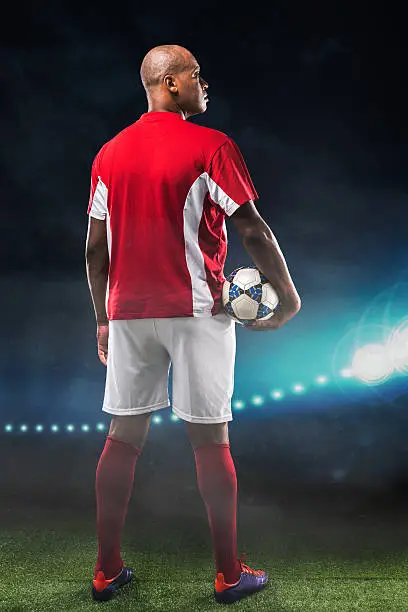 Confident soccer-player standing on the field, rear view