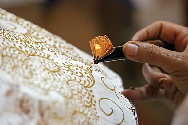 A woman uses a canting to apply wax to a cloth to make a pattern on a batik. Batik is a traditional form of decorating cloth, and Java is particularly famous for its variety of patterns and the quality of workmanship. The technique includes the manual application of wax between each dye bath to add each layer of colour individually.