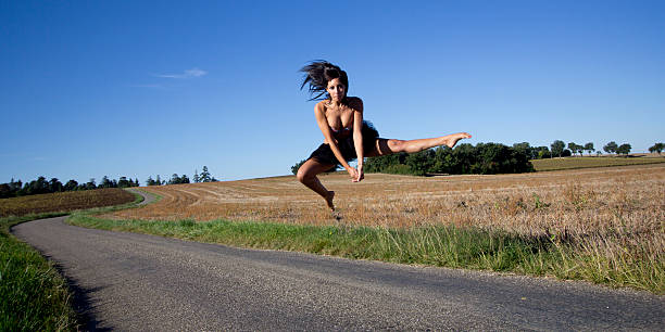 Spectacular jump of a barefoot dancer on a road. Spectacular jump of a dancer over a country road. She is barefoot and one of her legs is extended. Stubble in the background and blue sky. horse jumping front stock pictures, royalty-free photos & images